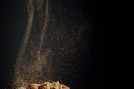 Fascio di bastoncini di cannella con polvere che si solleva su sfondo scuro.